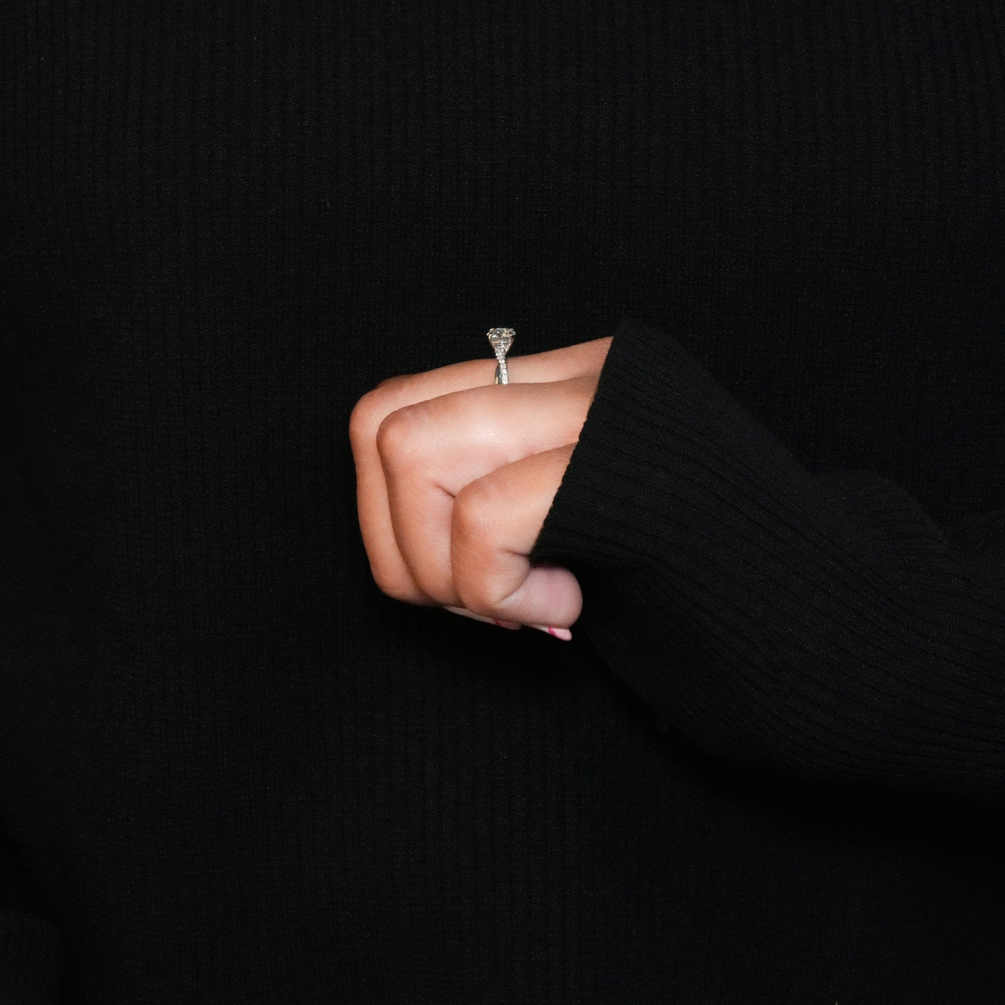 Ring with round clear center stone, twisted white metal band with pavé-set shoulders, side profile worn on a hand

