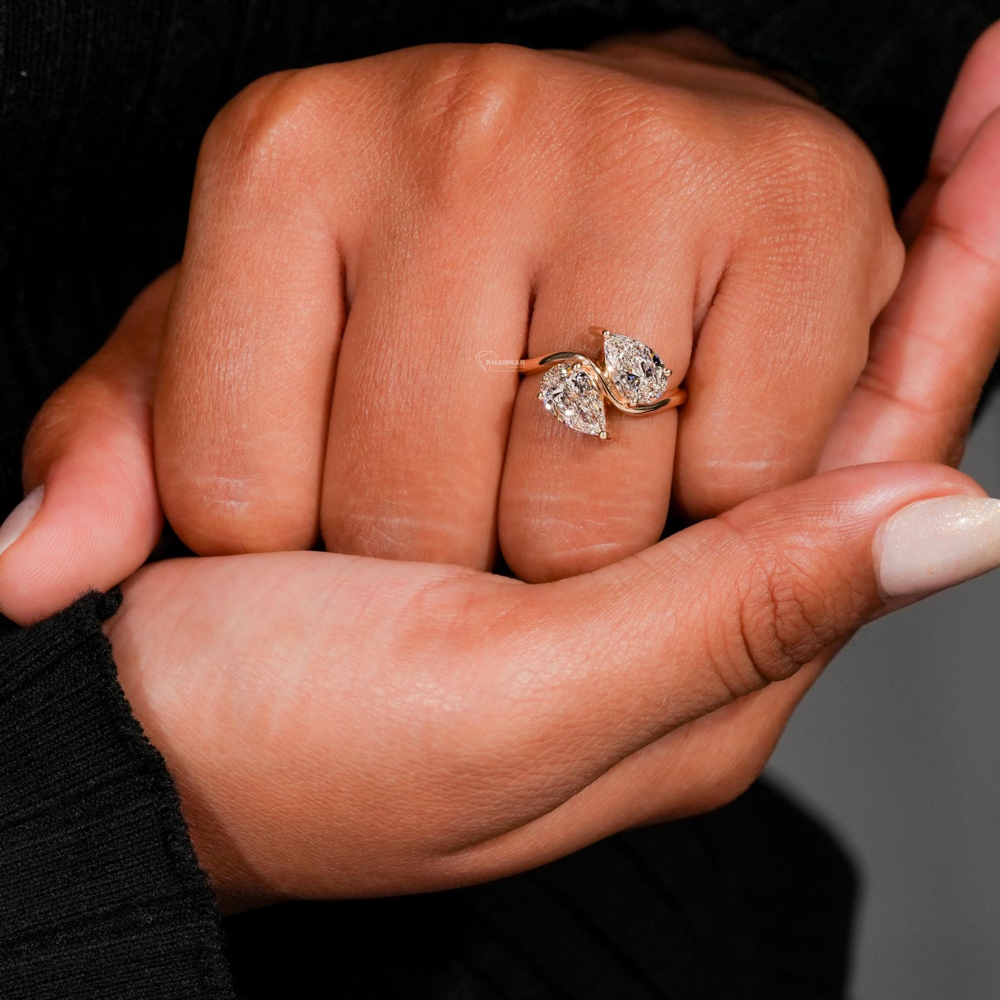Engagement ring with yellow metal bypass band, two pear-shaped clear gemstones, worn on finger, close-up front view
