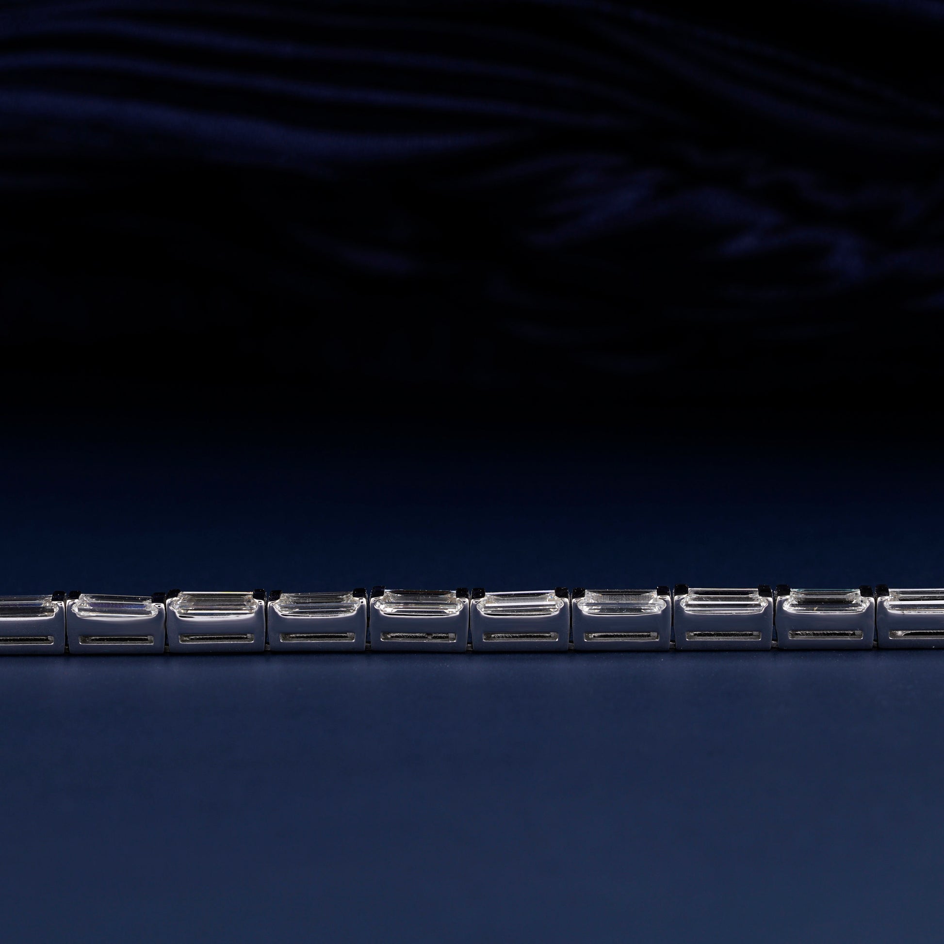Bracelet with white metal links, rectangular step-cut stones in tennis bracelet design, close-up horizontal detail view on a dark background
