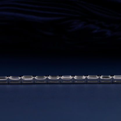 Bracelet with white metal links, rectangular step-cut stones in tennis bracelet design, close-up horizontal detail view on a dark background
