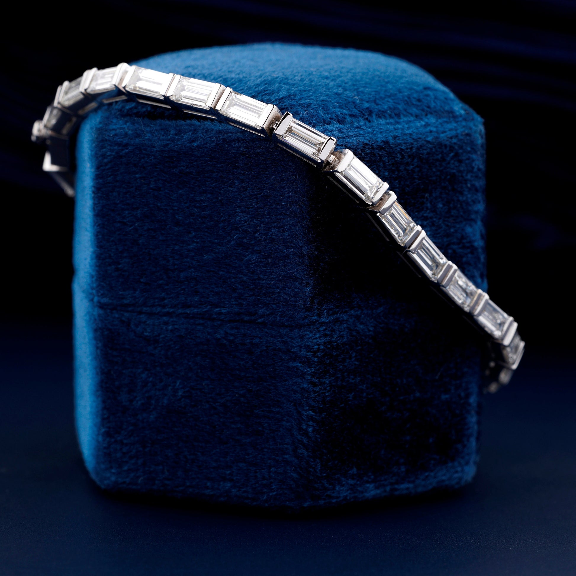 Bracelet with white metal links, rectangular step-cut stones in tennis bracelet design, displayed on a blue velvet stand, angled side view
