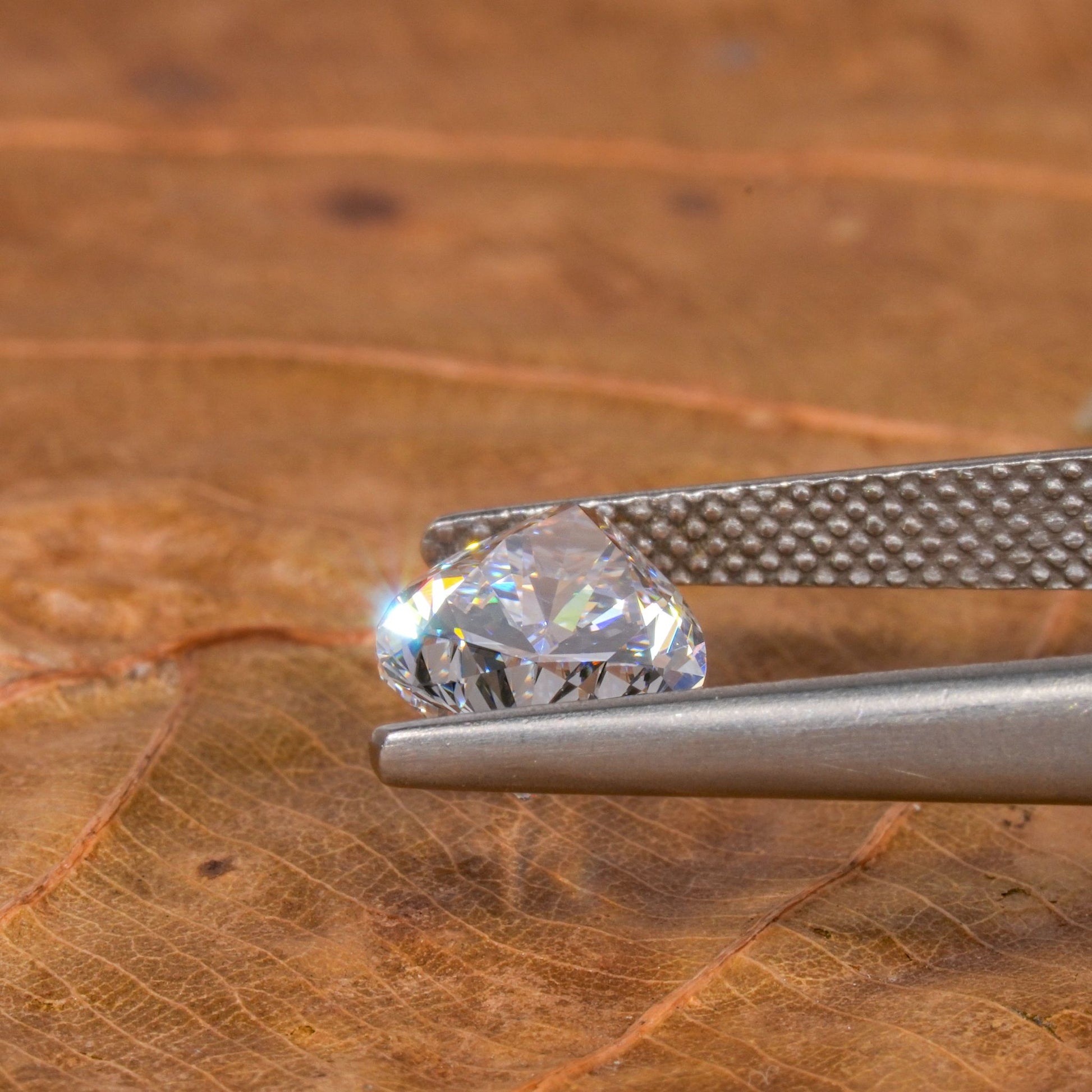 Loose pear-cut diamond, clear faceted gemstone held with tweezers on a leaf surface, side profile showing pavilion and pointed tip
