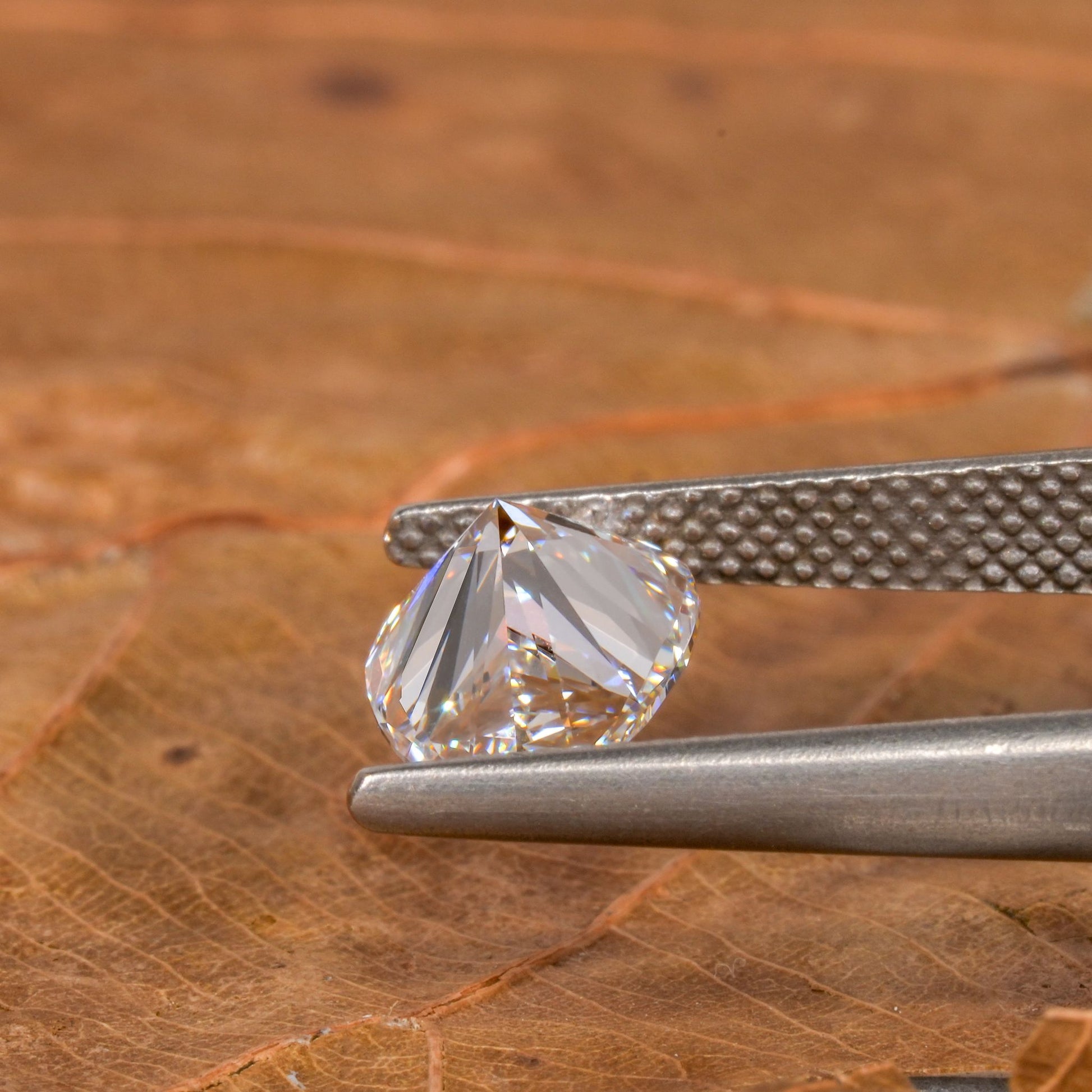 Loose pear-cut diamond, clear faceted gemstone held with tweezers on a leaf surface, angled pavilion view with pointed tip and rounded base
