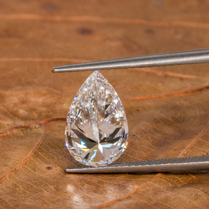 Loose pear-cut diamond, clear faceted gemstone held with tweezers on a leaf surface, front view with pointed tip and rounded base
