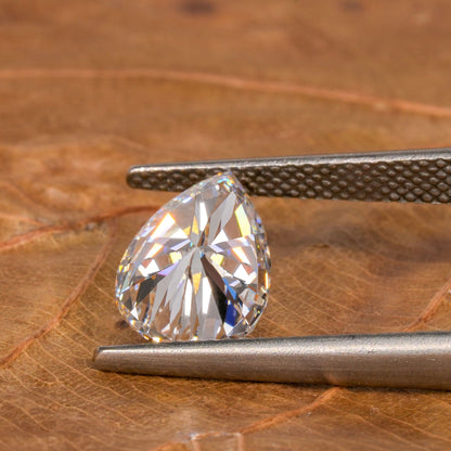 Loose pear-cut diamond, clear faceted gemstone held with tweezers on a leaf surface, pavilion view with pointed tip and rounded base
