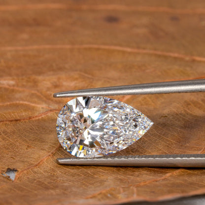 Loose pear-cut diamond, clear faceted gemstone held with tweezers on a leaf surface, horizontal top view with pointed tip and rounded end
