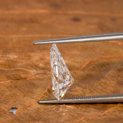 Loose pear-cut diamond, clear faceted gemstone held with tweezers on a leaf surface, side profile showing pavilion depth and pointed tip
