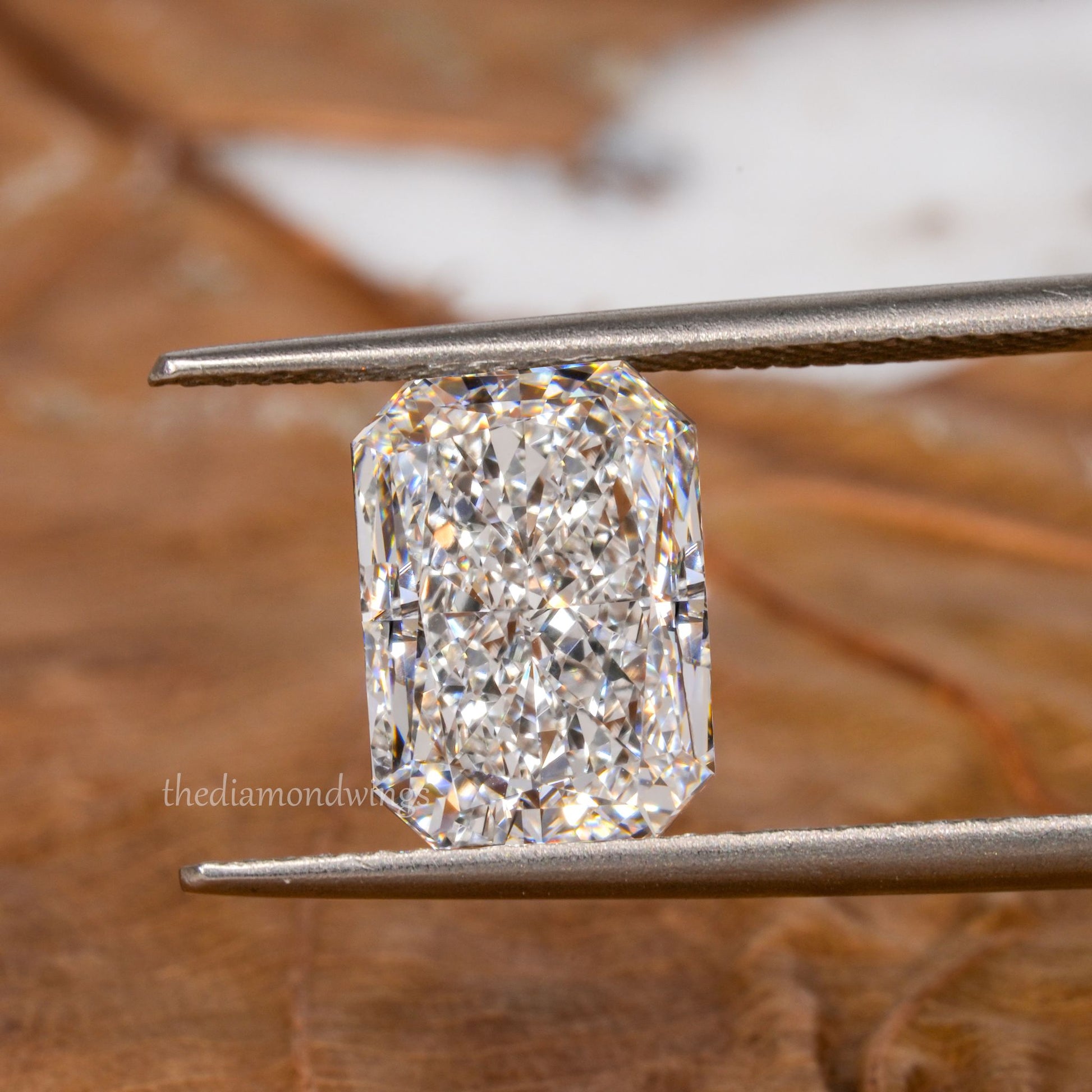 Loose radiant-cut diamond, clear faceted gemstone held with tweezers, face-up view with partial watermark visible
