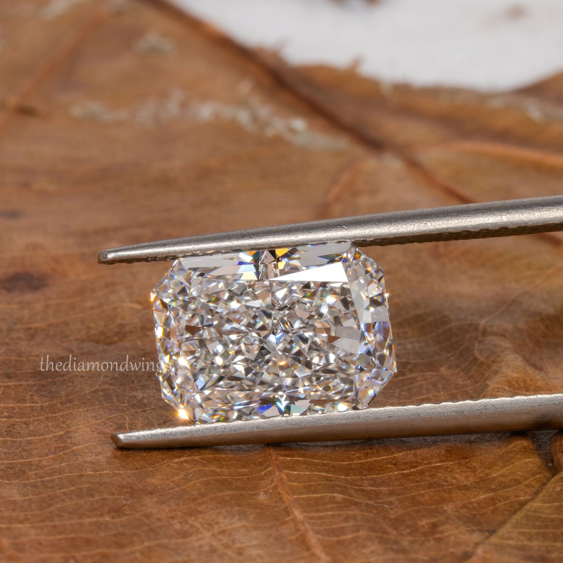 Loose radiant-cut diamond, clear faceted gemstone held with tweezers, horizontal face-up view with partial watermark visible
