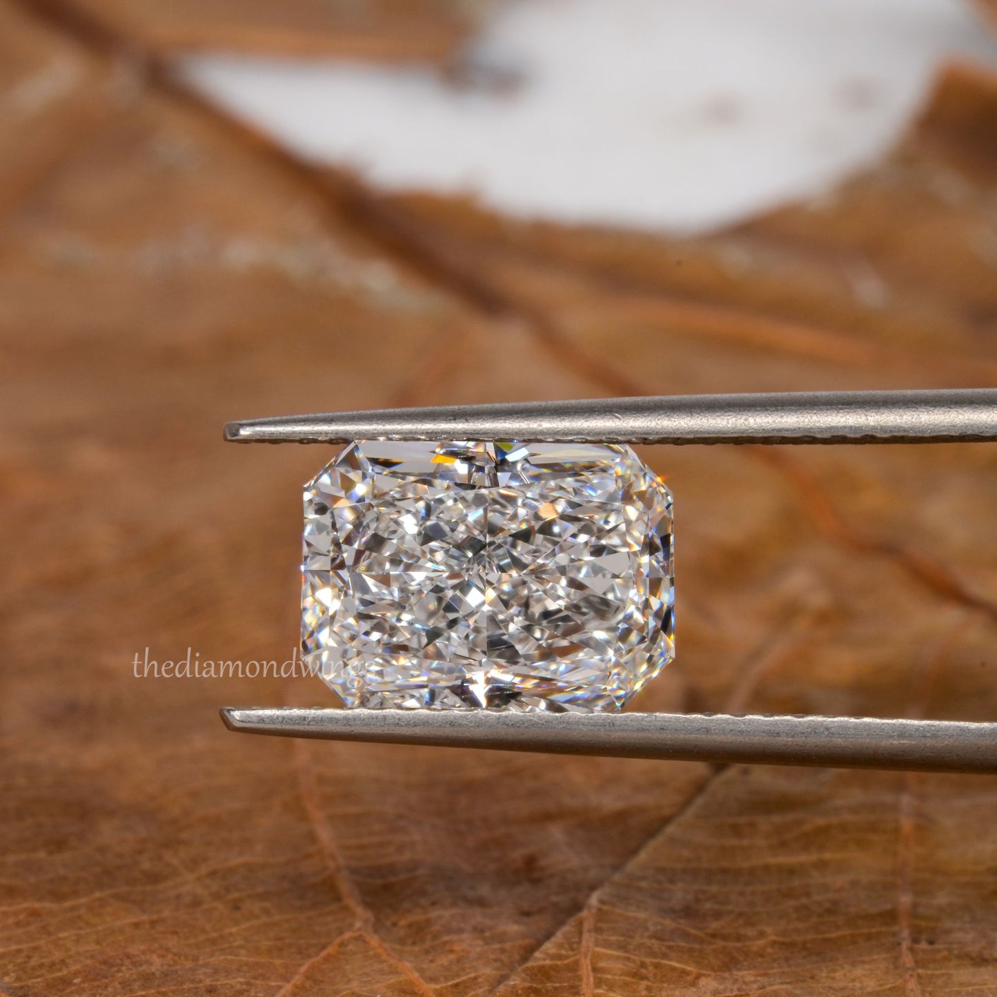 Loose cushion-cut diamond, clear faceted gemstone held with tweezers, face-up view with partial watermark visible
