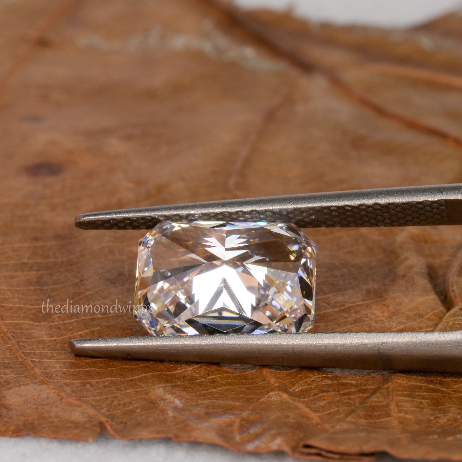 Loose cushion-cut diamond, clear faceted gemstone held with tweezers, pavilion view showing underside facets with partial watermark visible
