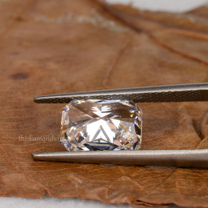 Loose cushion-cut diamond, clear faceted gemstone held with tweezers, pavilion view showing underside facets with partial watermark visible
