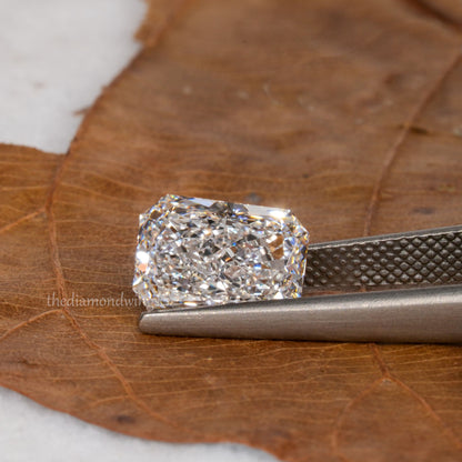 Loose cushion-cut diamond, clear faceted gemstone held with tweezers, angled face-up view with partial watermark visible
