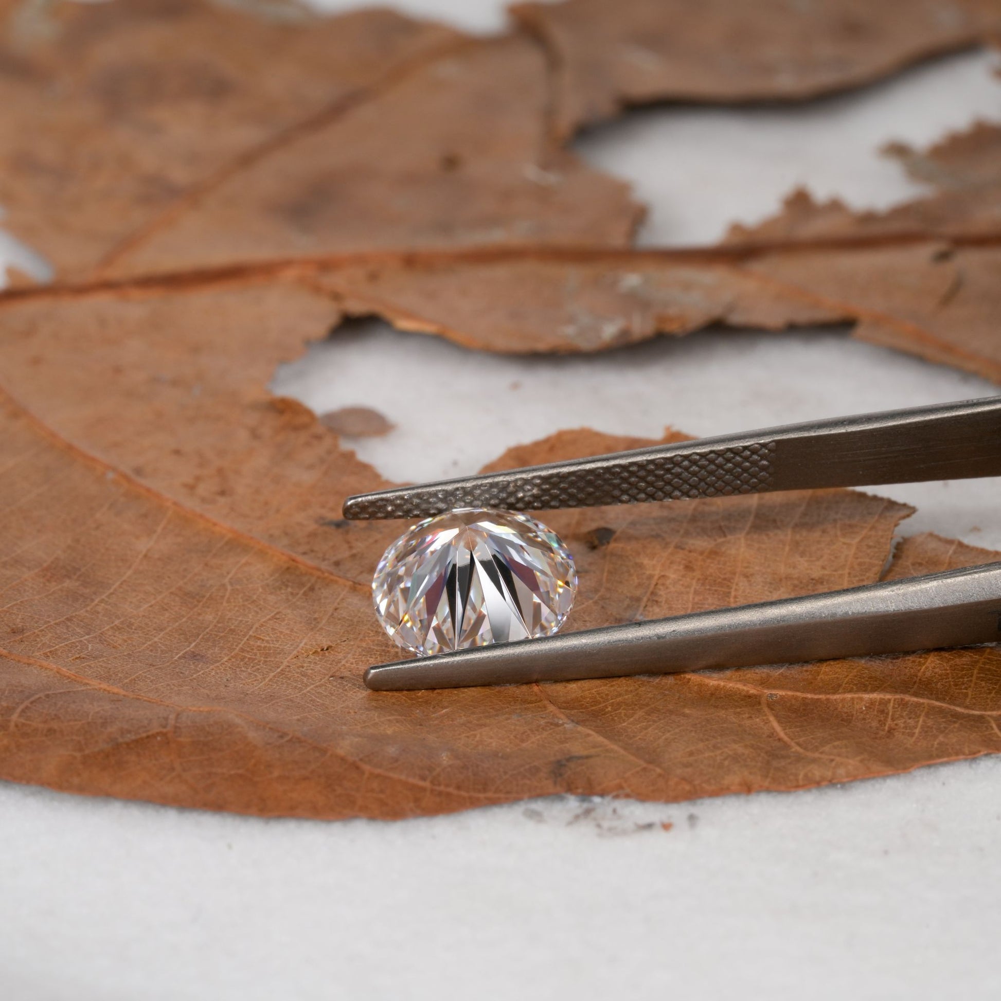 Loose round brilliant-cut diamond held with tweezers, faceted clear stone, side profile view
