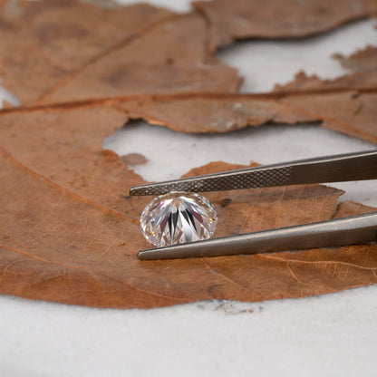 Loose round brilliant-cut diamond held with tweezers, faceted clear stone, side profile view
