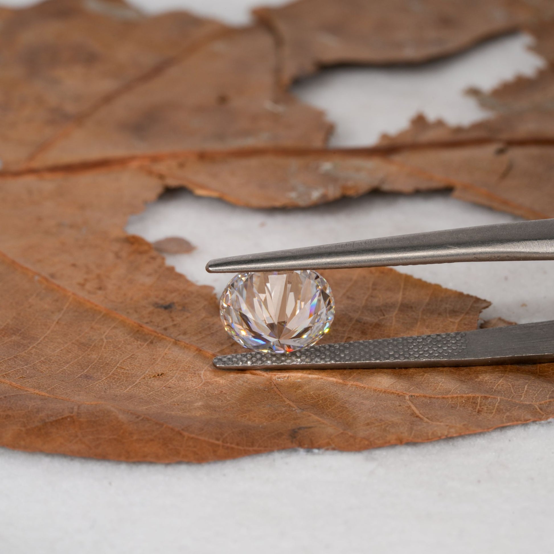 Loose round brilliant-cut diamond held with tweezers, faceted clear stone, side profile view with pavilion visible
