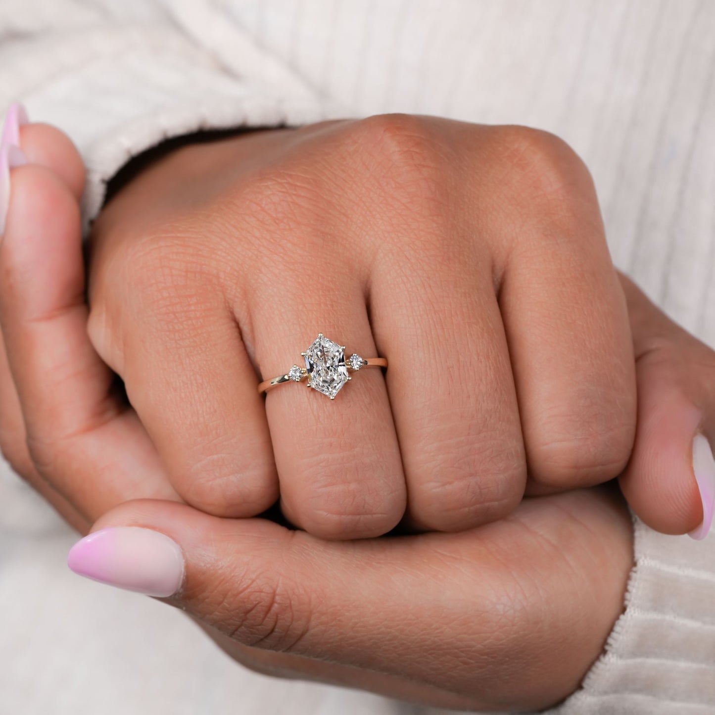 Ring with hexagonal clear center stone, two round side stones and slim gold-tone band, shown worn on a hand
