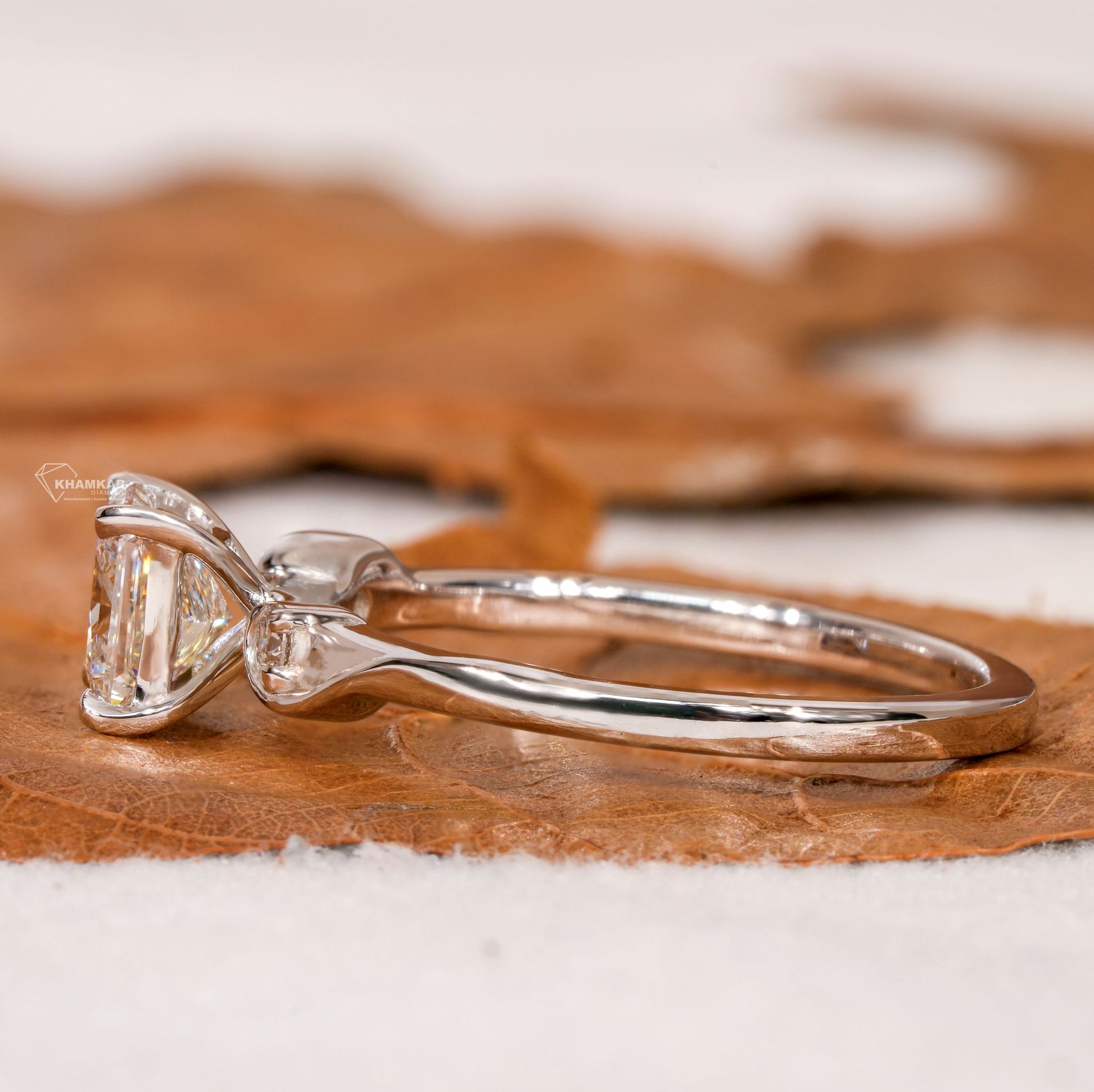 Ring with clear square center stone and raised side setting on a polished silver-tone curved band, side view

