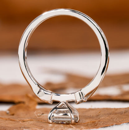 Ring with polished silver-tone band and raised clear stone setting, shown from the rear view on a brown leaf surface
