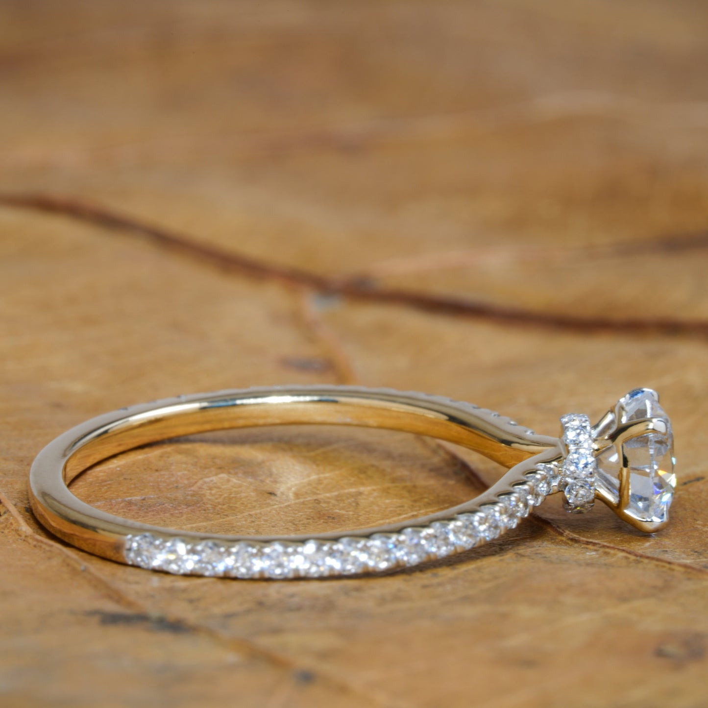 Engagement ring with round clear center stone, white metal pavé band and halo detail, side profile view on wooden surface
