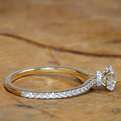 Engagement ring with round clear center stone, white metal pavé band and halo detail, side profile view on wooden surface
