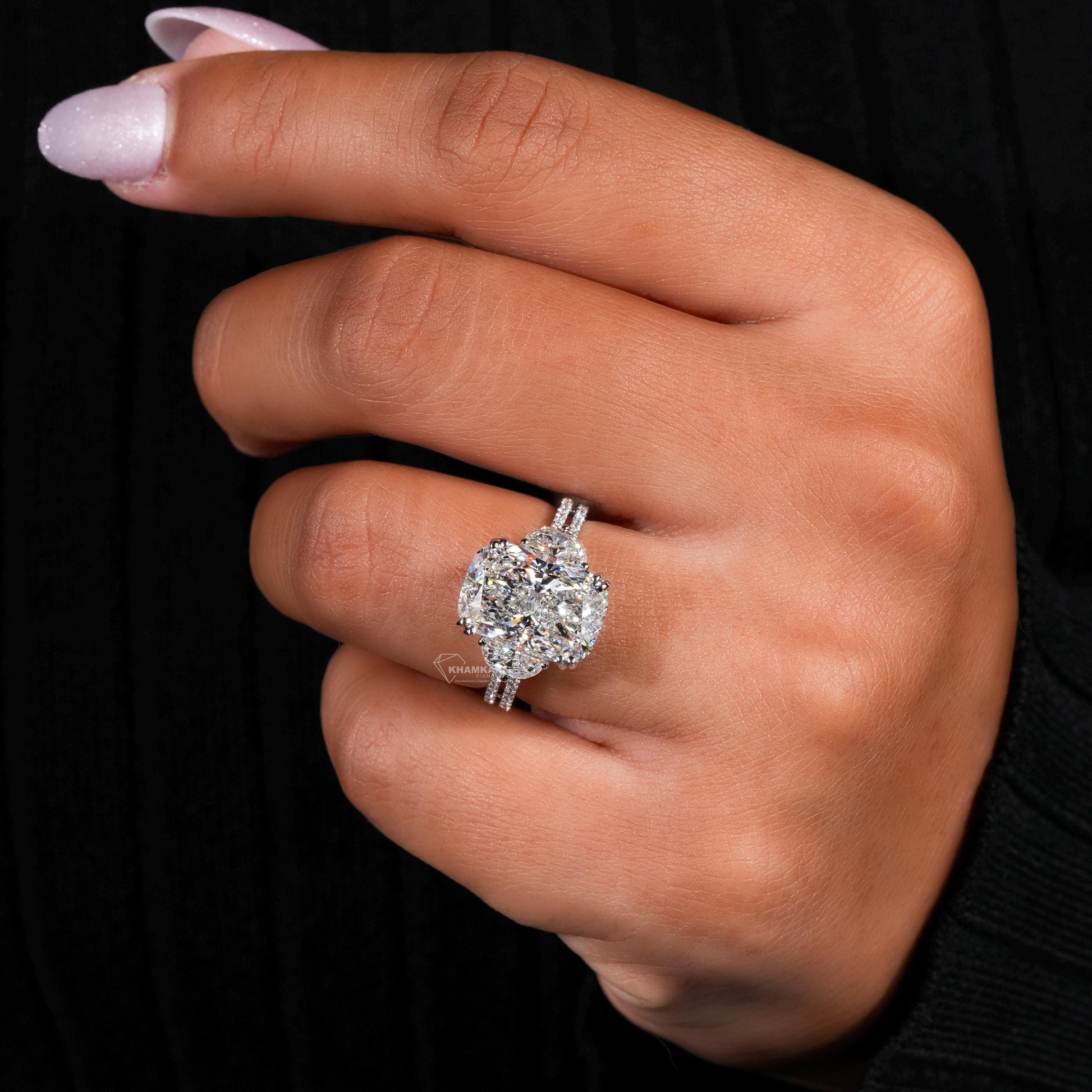 Engagement ring with white metal split shank, elongated cushion-cut clear center stone, halo setting, worn on finger, angled view
