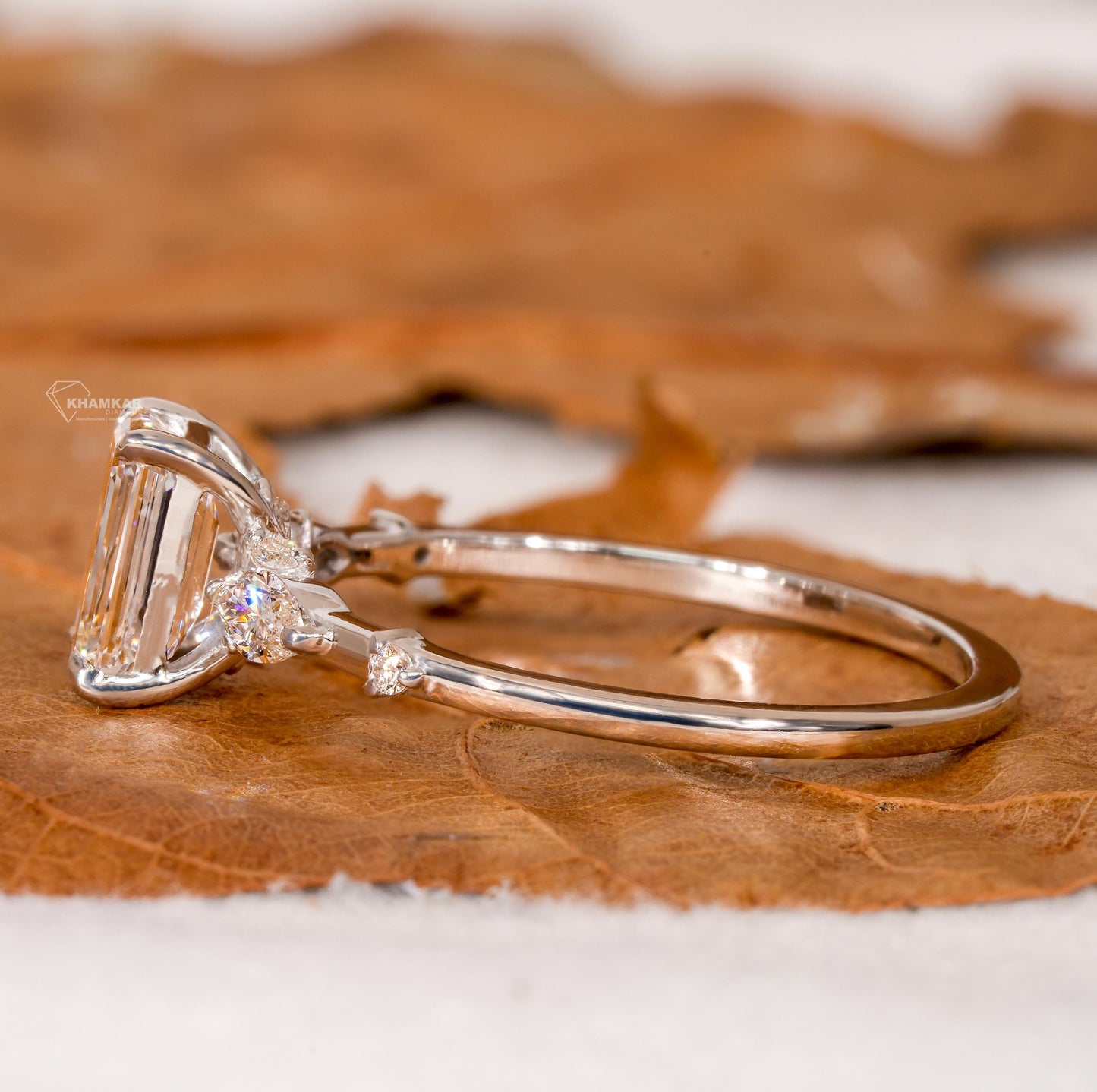 Engagement ring with white metal band, emerald-cut clear center stone, marquise side stones and round accents, side profile view
