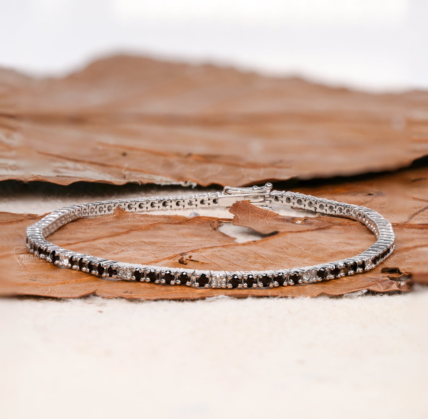 Bracelet with black and clear round stones in a continuous line setting, white metal, box clasp, front angled product view, tennis bracelet jewelry
