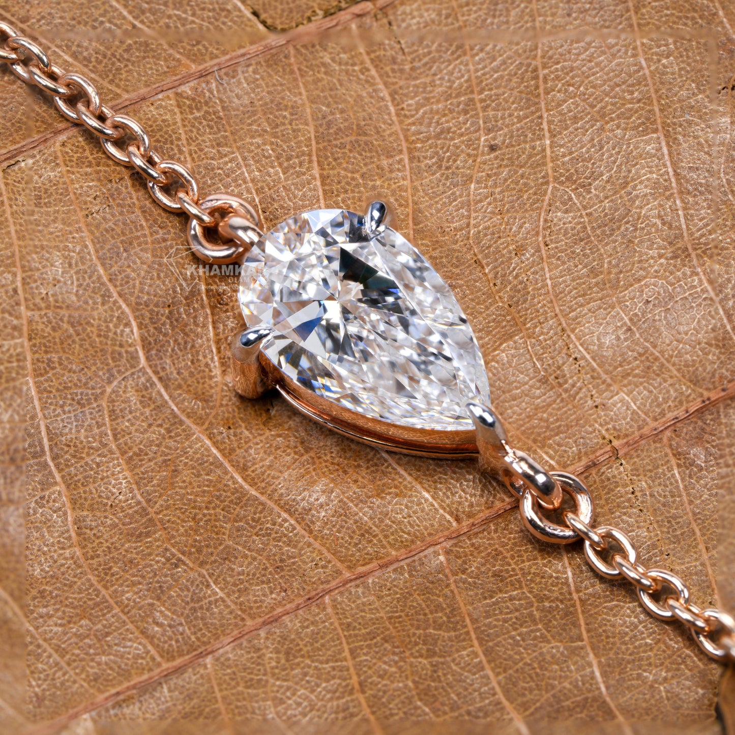Bracelet with pear-shaped clear stone in yellow metal chain setting on textured leaf, close-up top view, bracelet jewelry
