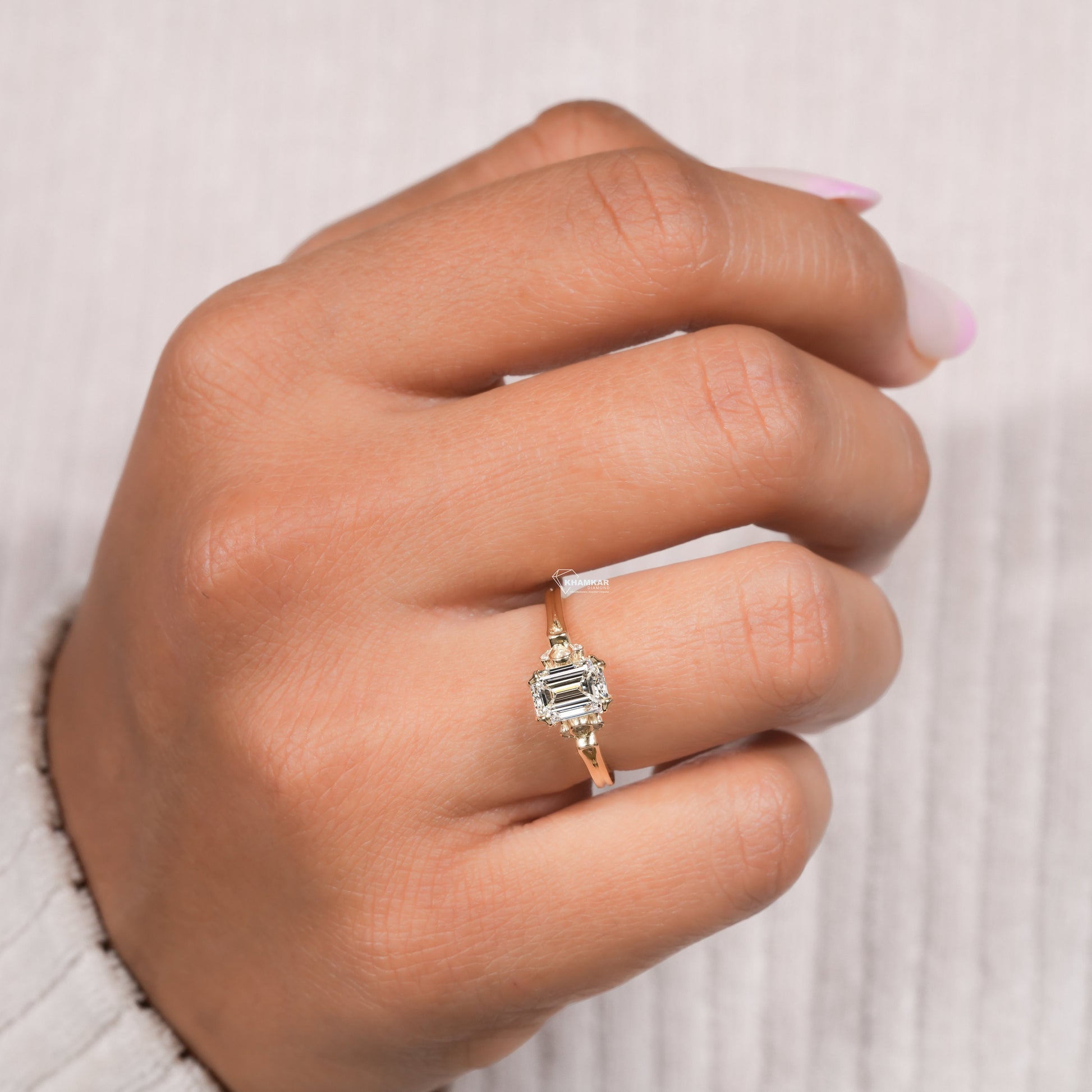 Engagement ring with rectangular clear gemstone, yellow metal band, halo design with round accent stones, worn on finger, angled top view
