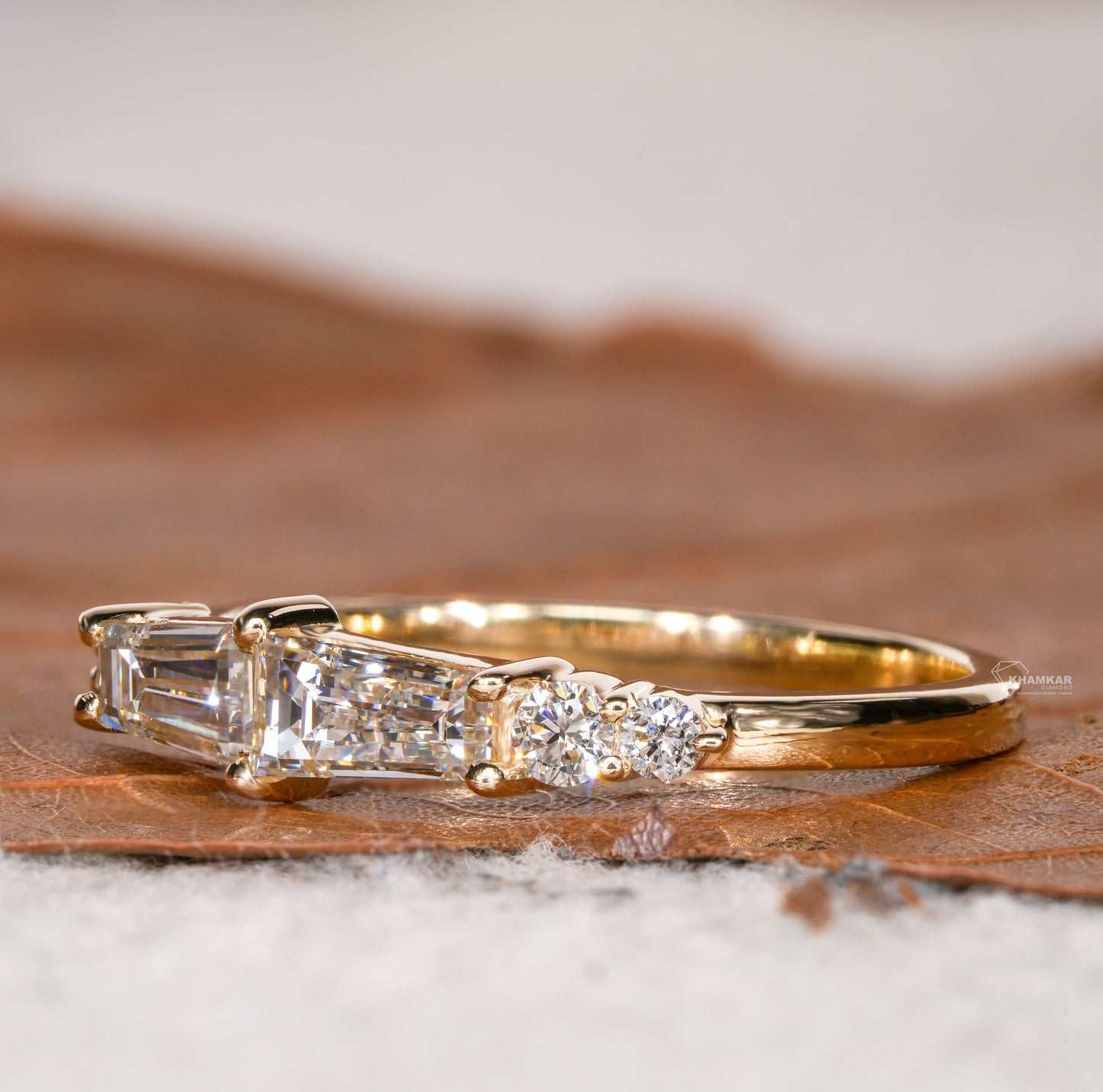 Engagement ring with yellow gold band, horizontal baguette-cut clear center gemstone and round side stones, side profile view
