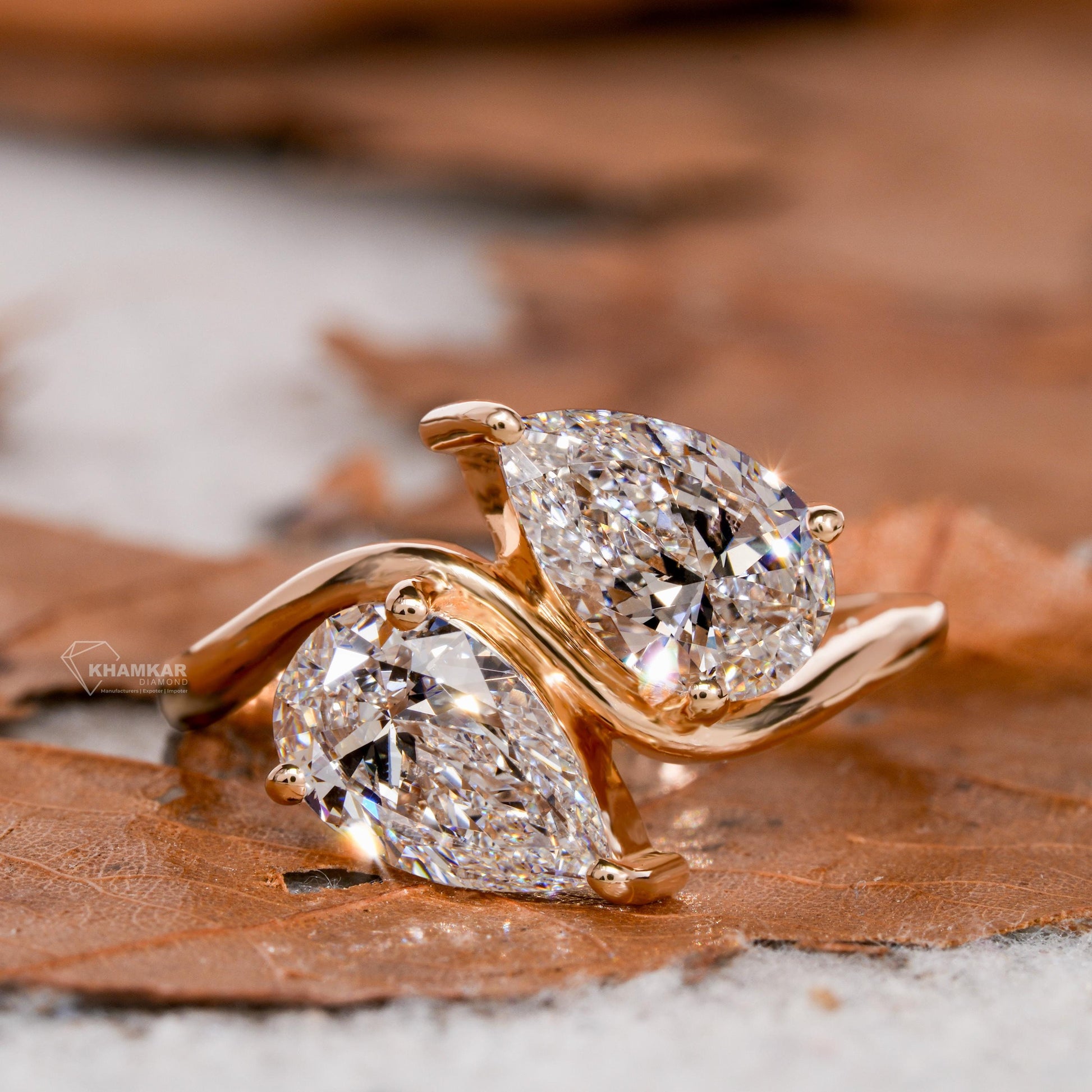 Engagement ring with yellow metal bypass band, two pear-shaped clear gemstones, open crossover design, angled close-up view
