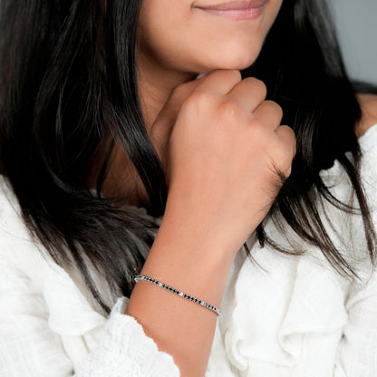 Bracelet with alternating black and clear round stones in a white metal line setting, worn on wrist, lifestyle close-up view, tennis bracelet jewelry
