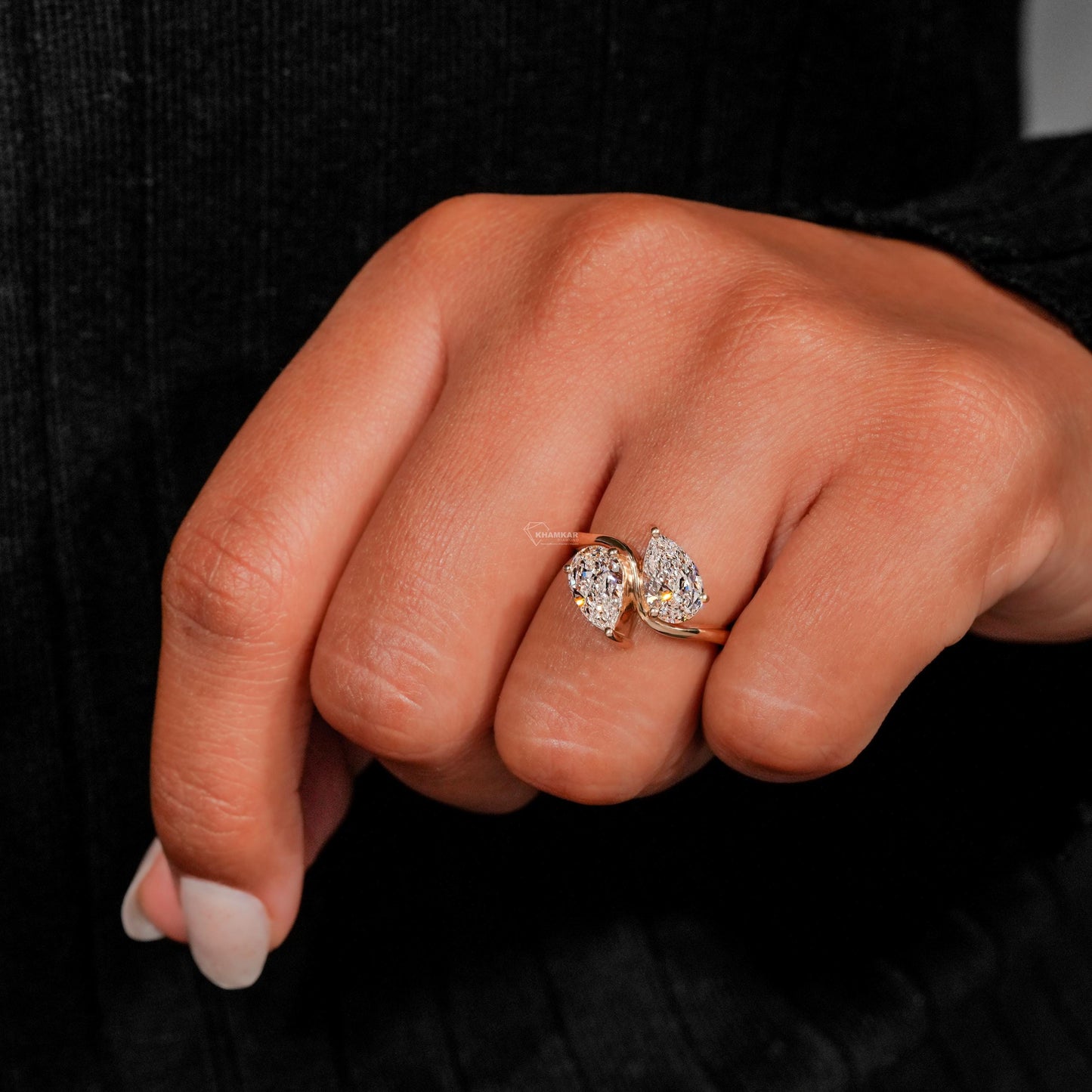 Engagement ring with yellow metal bypass band, two pear-shaped clear gemstones, worn on finger, top view

