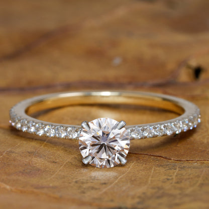 Engagement ring with round clear center stone, white metal pavé band, four-prong solitaire setting, front view on wooden surface
