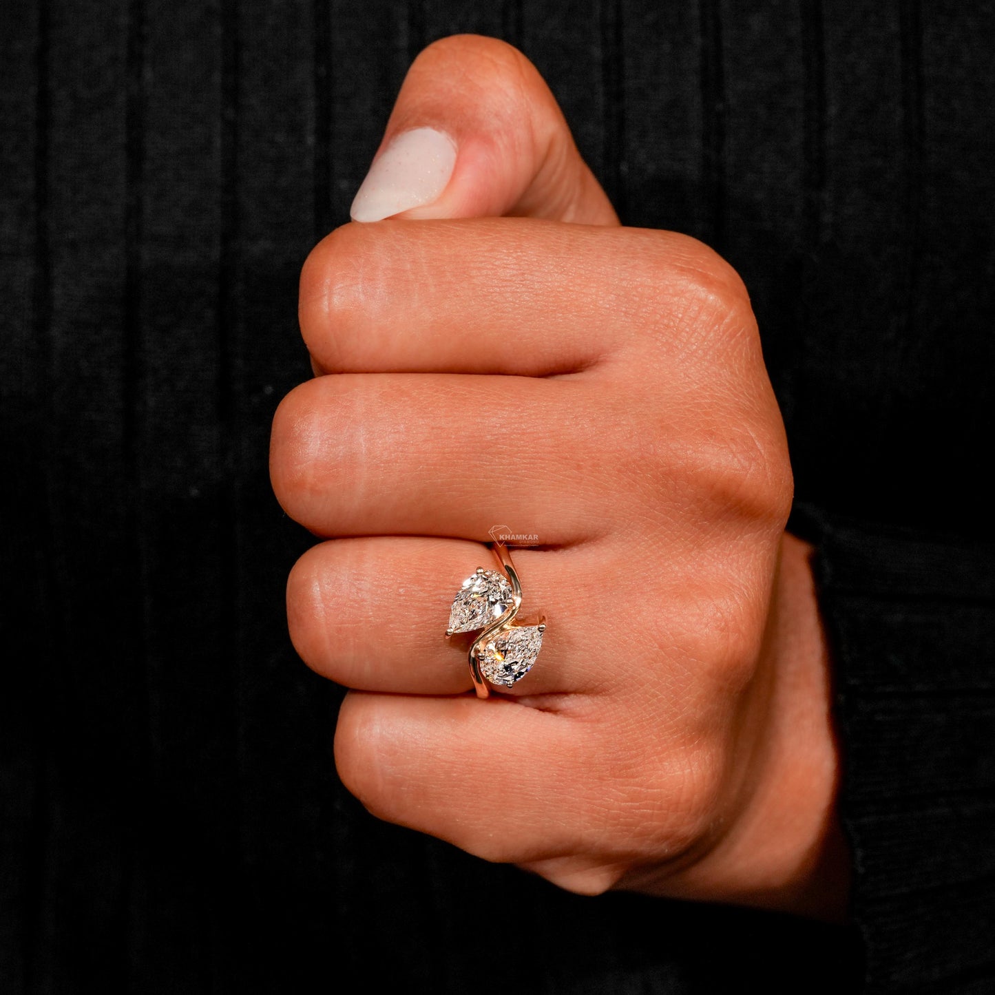 Engagement ring with yellow metal bypass band, two pear-shaped clear gemstones, worn on finger, front view
