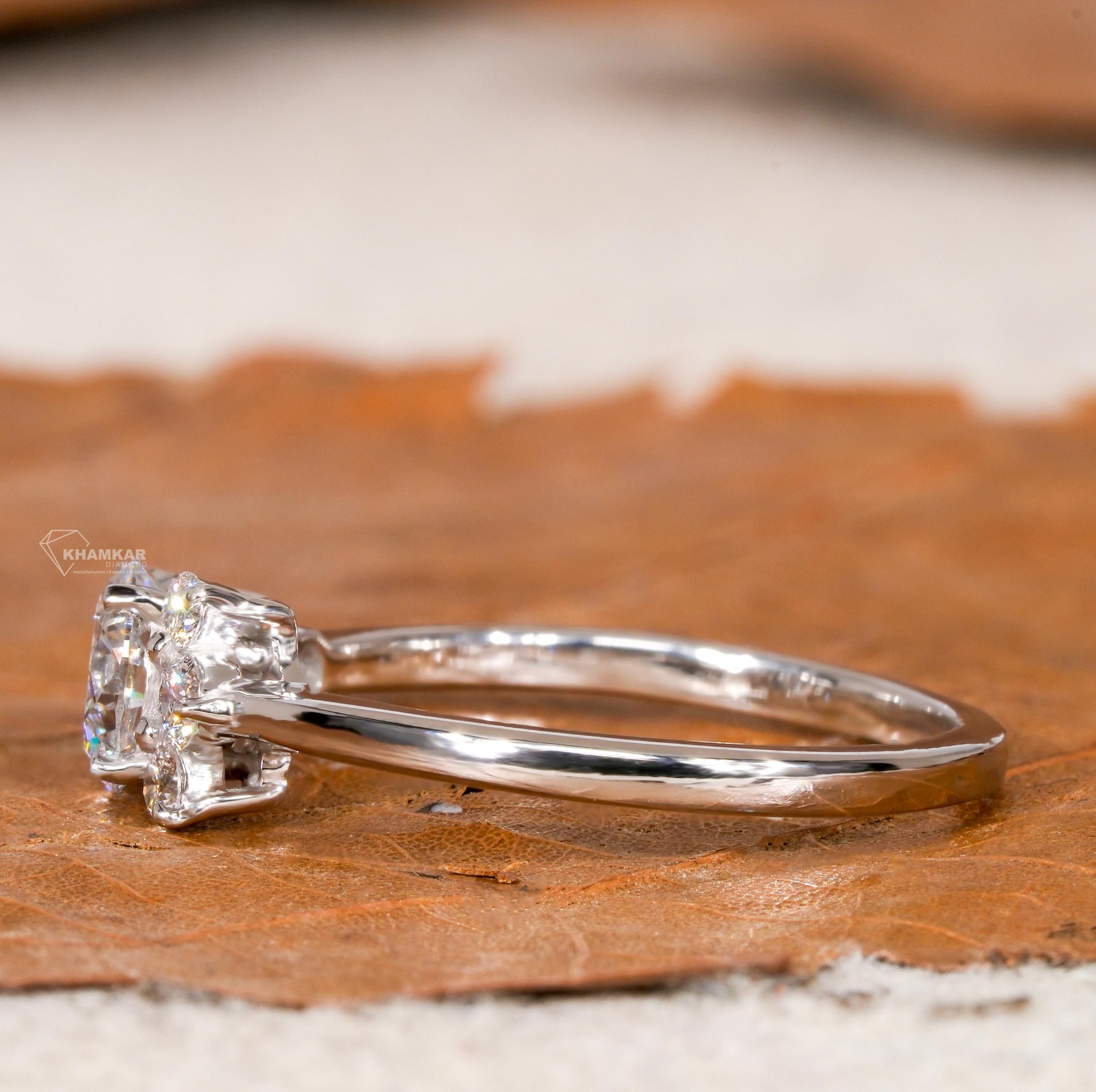 Engagement ring with white metal, round center stone, round accent diamond cluster setting, side profile view

