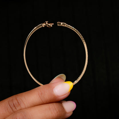 Bracelet with yellow metal band, slim round stone tennis design, open clasp detail, held between fingers, front view against a black background
