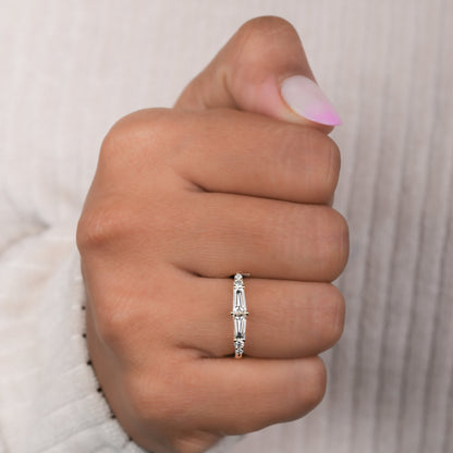 Engagement ring with yellow gold band, vertical baguette-cut clear center gemstone and round side stones, worn on finger, front view
