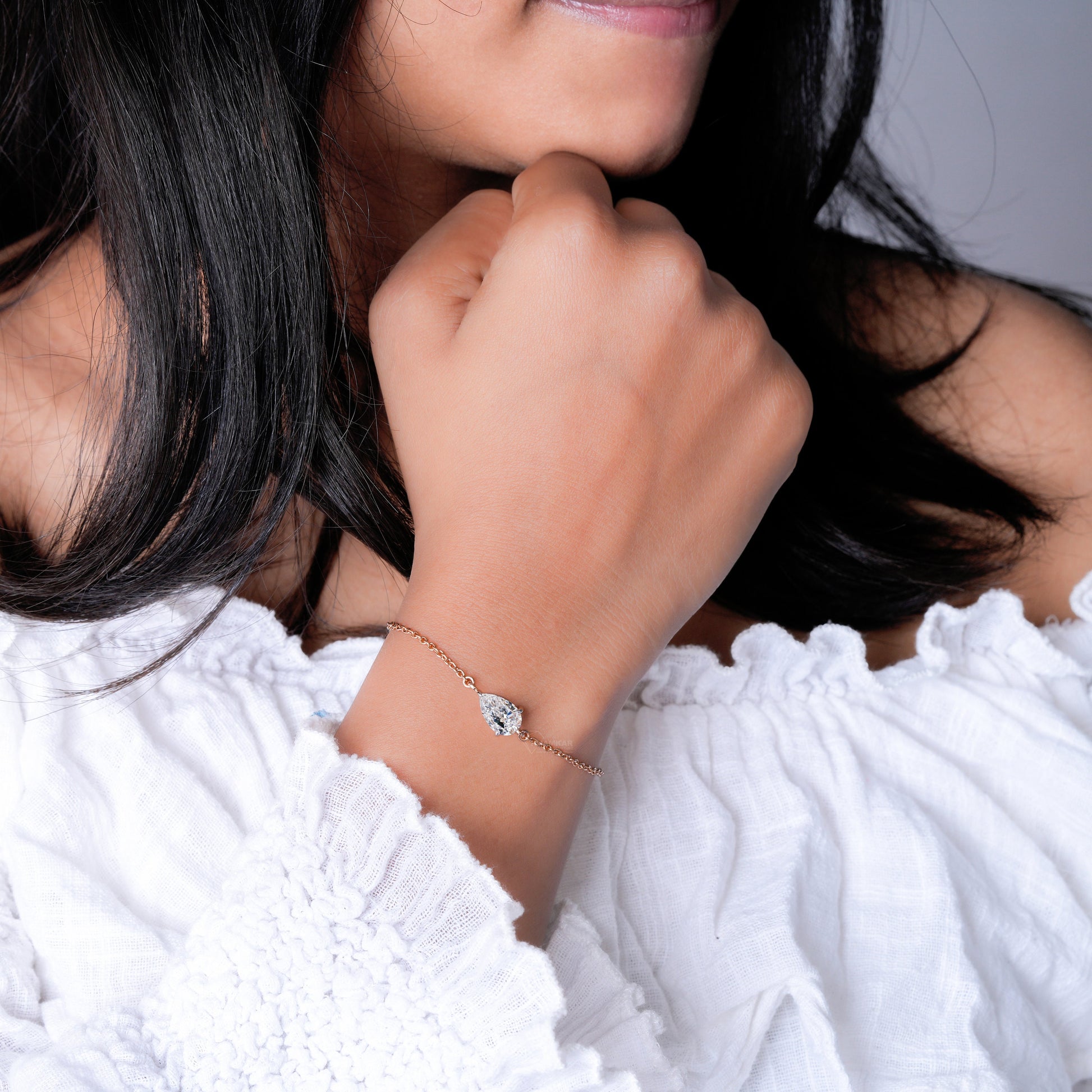 Bracelet with pear-shaped clear stone on yellow metal chain, worn on wrist, close-up lifestyle view, delicate chain bracelet jewelry
