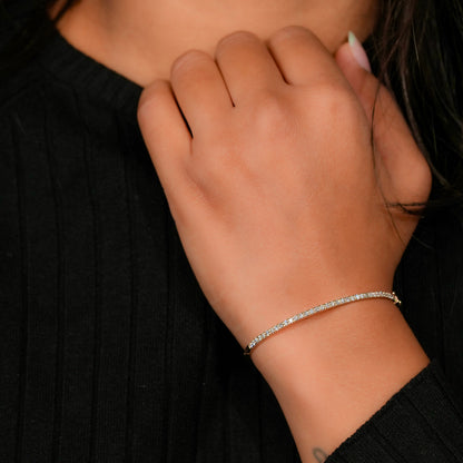 Bracelet with yellow metal band, slim round stone tennis design, worn on wrist, angled front view against a black knit top background
