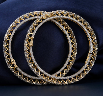 Bracelets with yellow metal bands, heart-shaped stone tennis design, overlapping pair with clasp detail, front view against a dark blue fabric background
