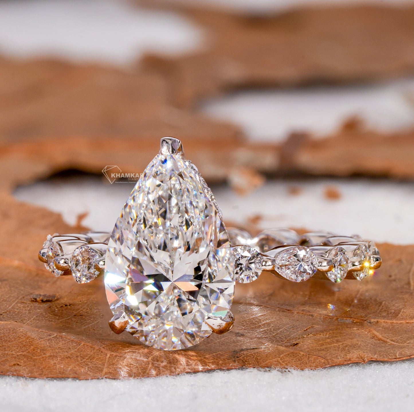 Engagement ring with polished white metal band, pear-shaped clear gemstone and round accent stones, front angled view
