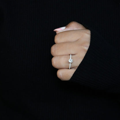 Engagement ring with round clear center stone, white metal pavé band, worn on hand, front-facing view
