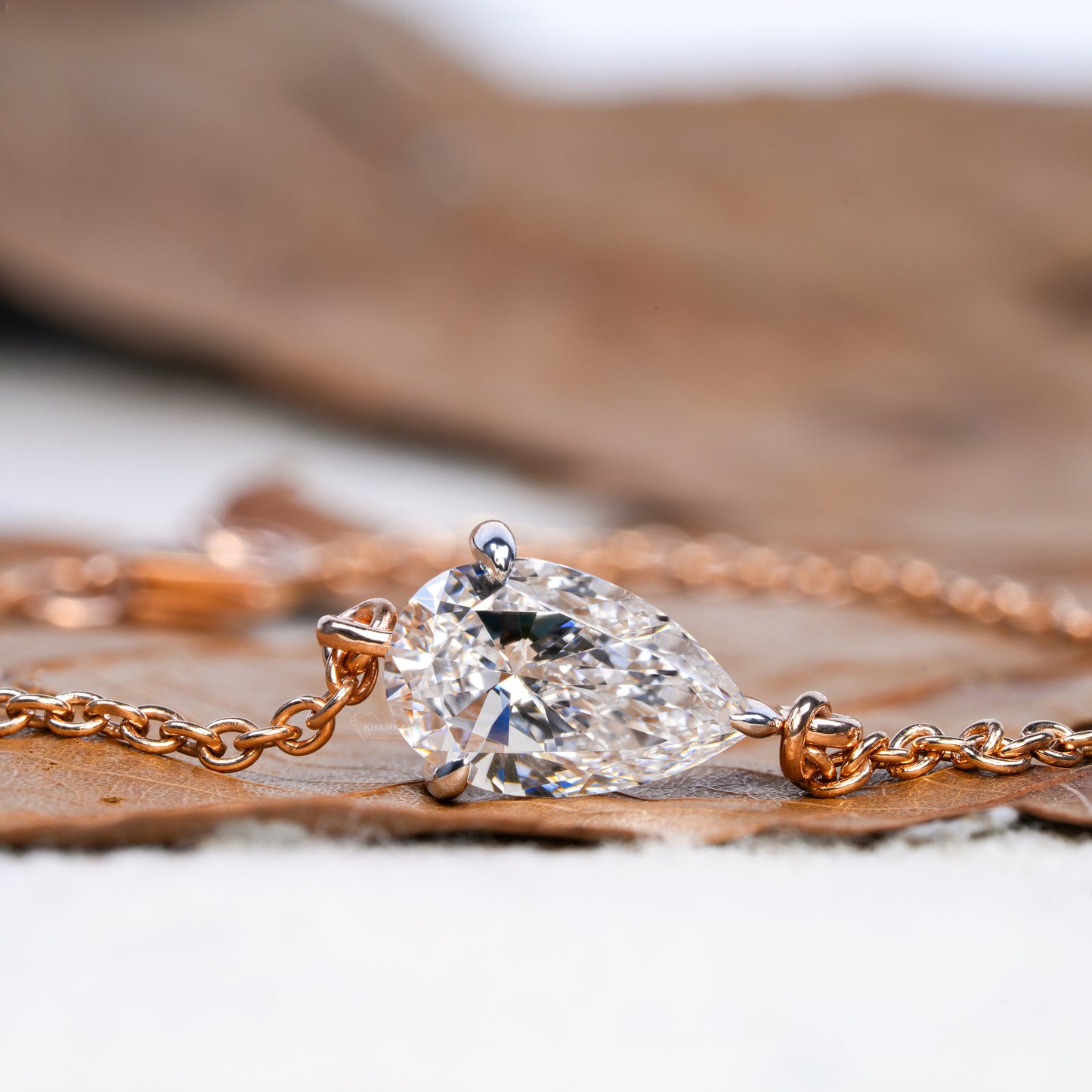 Bracelet with pear-shaped clear stone in yellow metal chain setting, side profile close-up on leaf surface, bracelet jewelry
