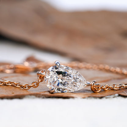 Bracelet with pear-shaped clear stone in yellow metal chain setting, side profile close-up on leaf surface, bracelet jewelry
