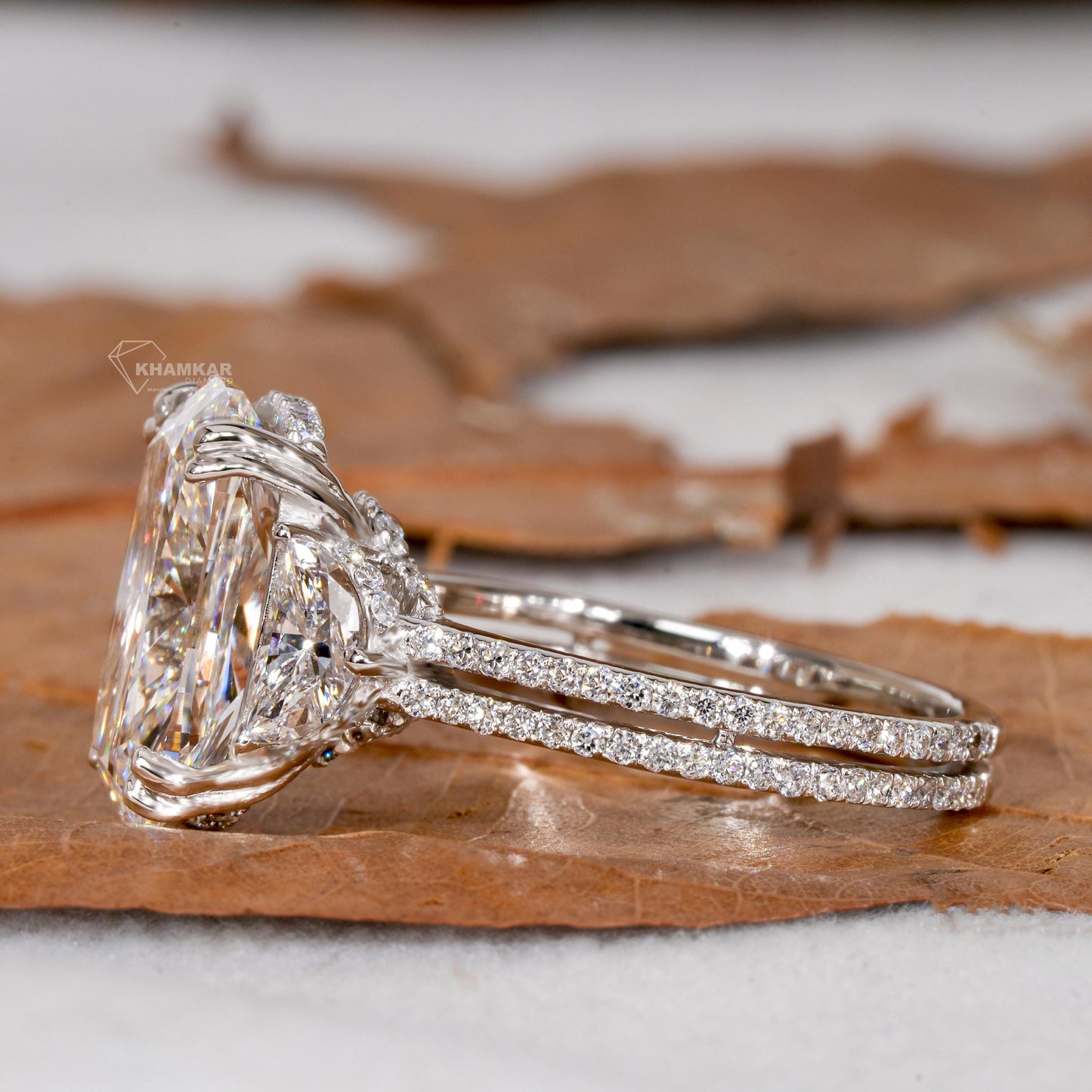 Engagement ring with white metal split shank, elongated cushion-cut clear center stone, oval side stones, side profile view
