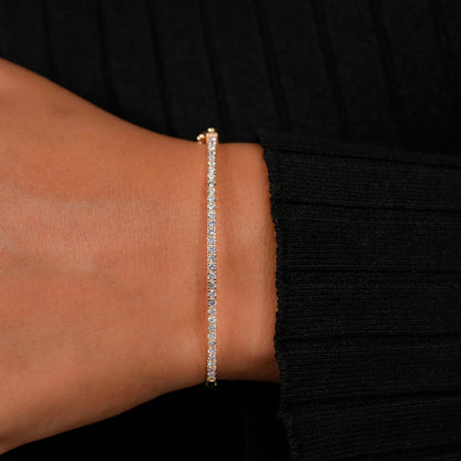 Bracelet with yellow metal band, slim round stone tennis design, worn on wrist, front view against a black sleeve background
