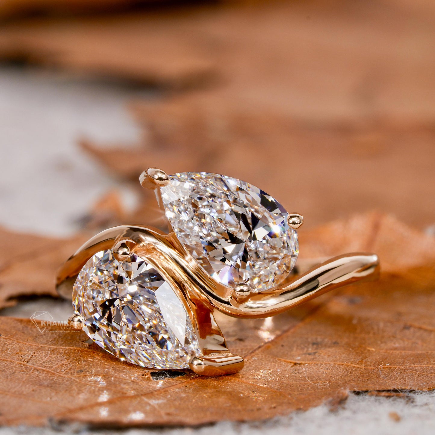 Engagement ring with yellow metal bypass band, two pear-shaped clear gemstones, crossover design, angled close-up view
