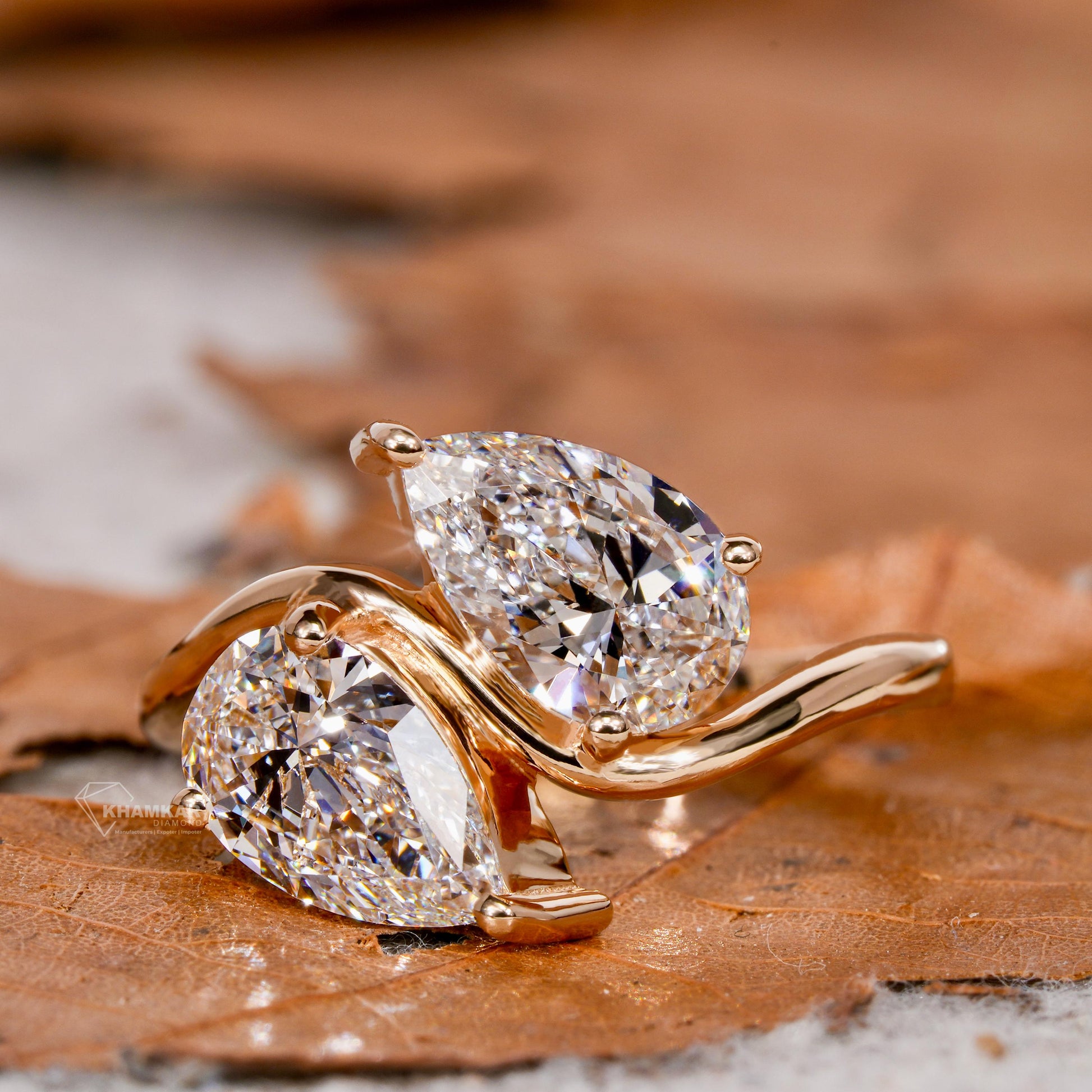 Engagement ring with yellow metal bypass band, two pear-shaped clear gemstones, crossover design, angled close-up view
